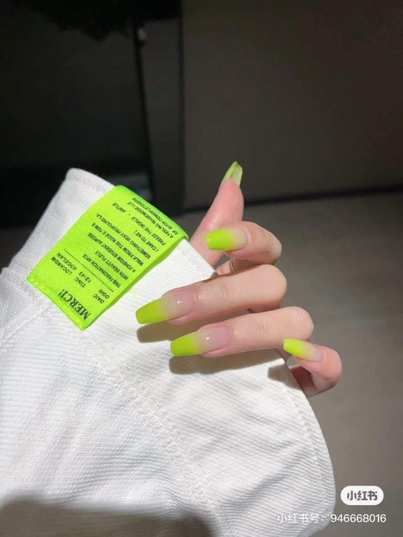 Tay với móng tay màu xanh neon cầm vải trắng có nhãn màu xanh lá cây.