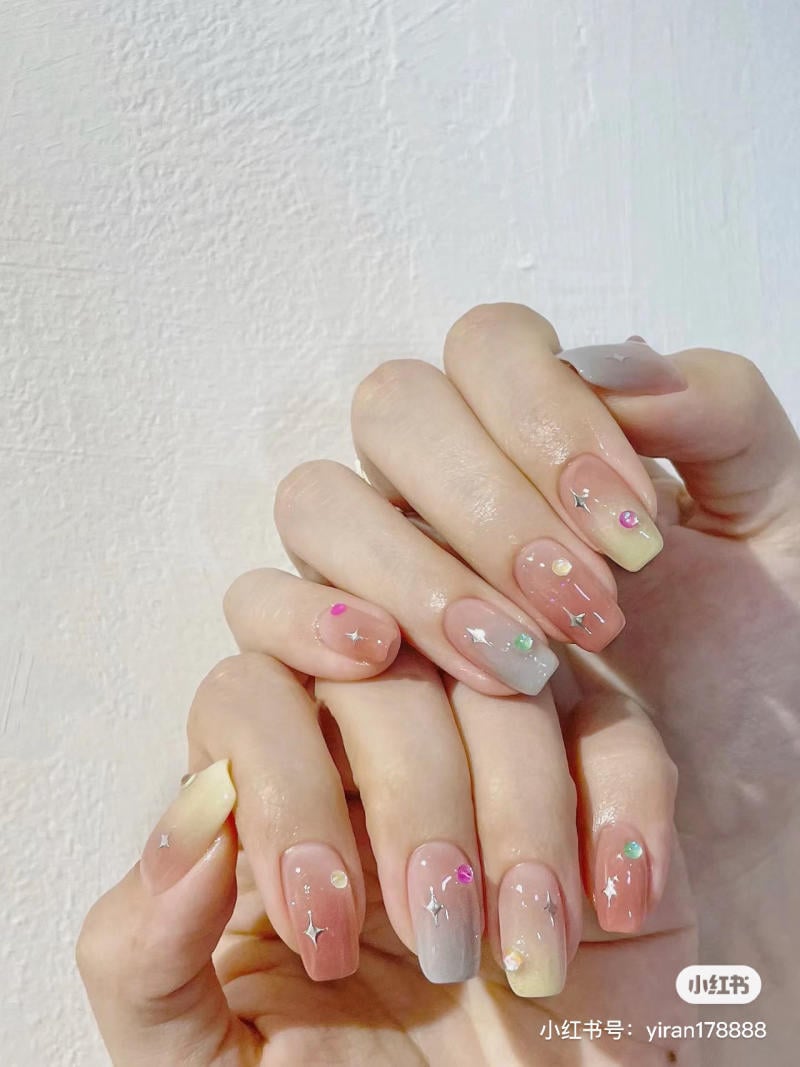 Bàn tay với móng tay sơn màu pastel, trang trí họa tiết lấp lánh và đính đá nhỏ, nền trắng.