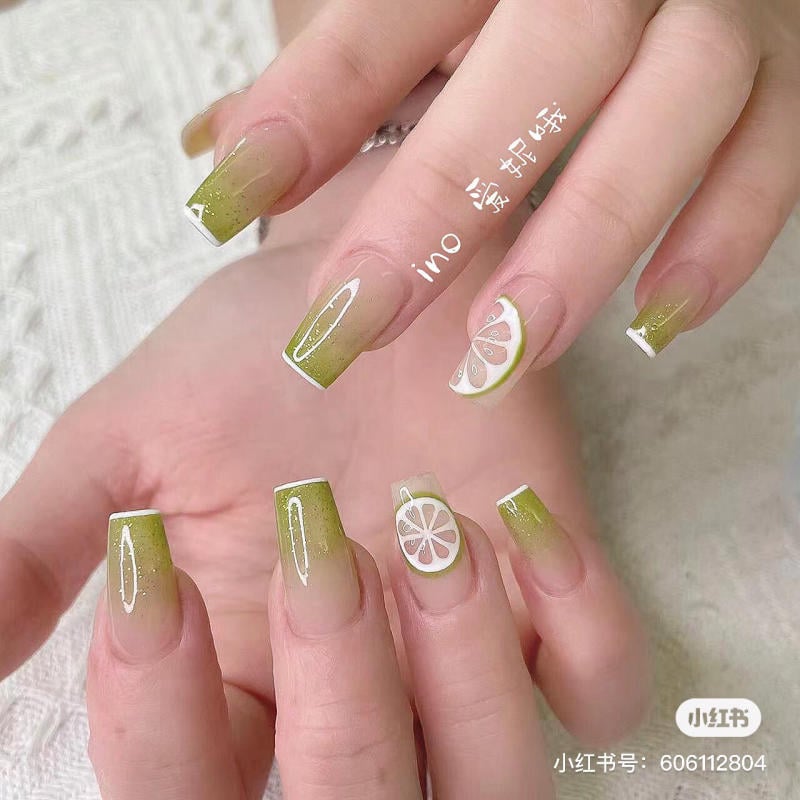 Bàn tay với móng tay sơn màu xanh và trang trí họa tiết chanh, nền vải trắng.