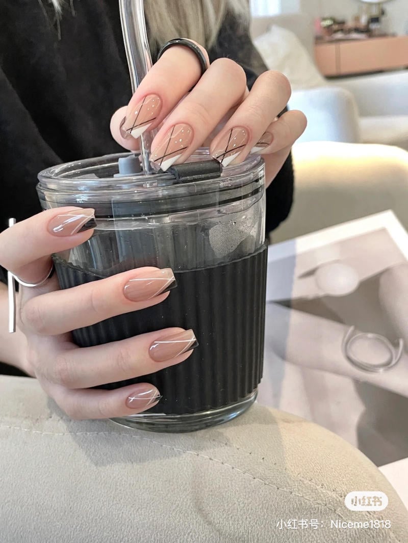 Bàn tay với móng tay được trang trí nghệ thuật, cầm ly nước màu đen trên nền ghế màu sáng.