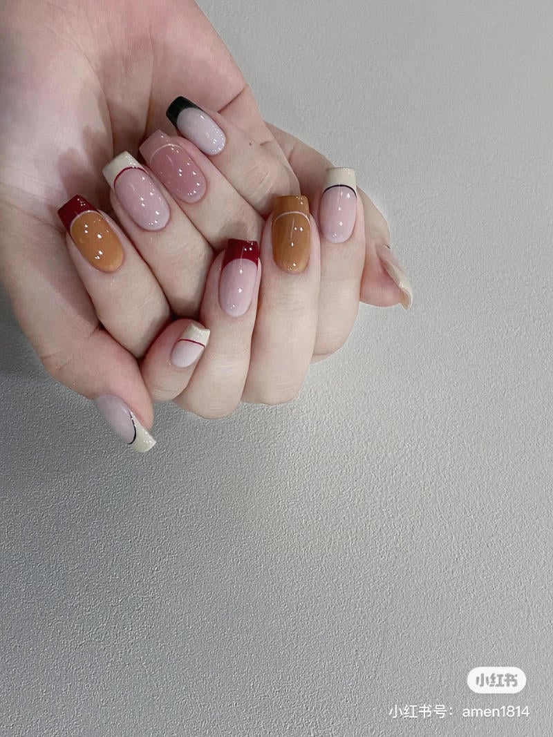 Bàn tay với móng tay được sơn màu sắc đa dạng, kết hợp giữa các tông màu nâu, đỏ và be, trên nền xám.