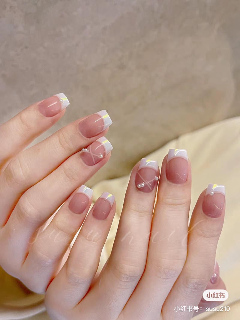 Bàn tay với móng tay được sơn kiểu Pháp, có đường viền trắng và trang trí hạt ngọc.