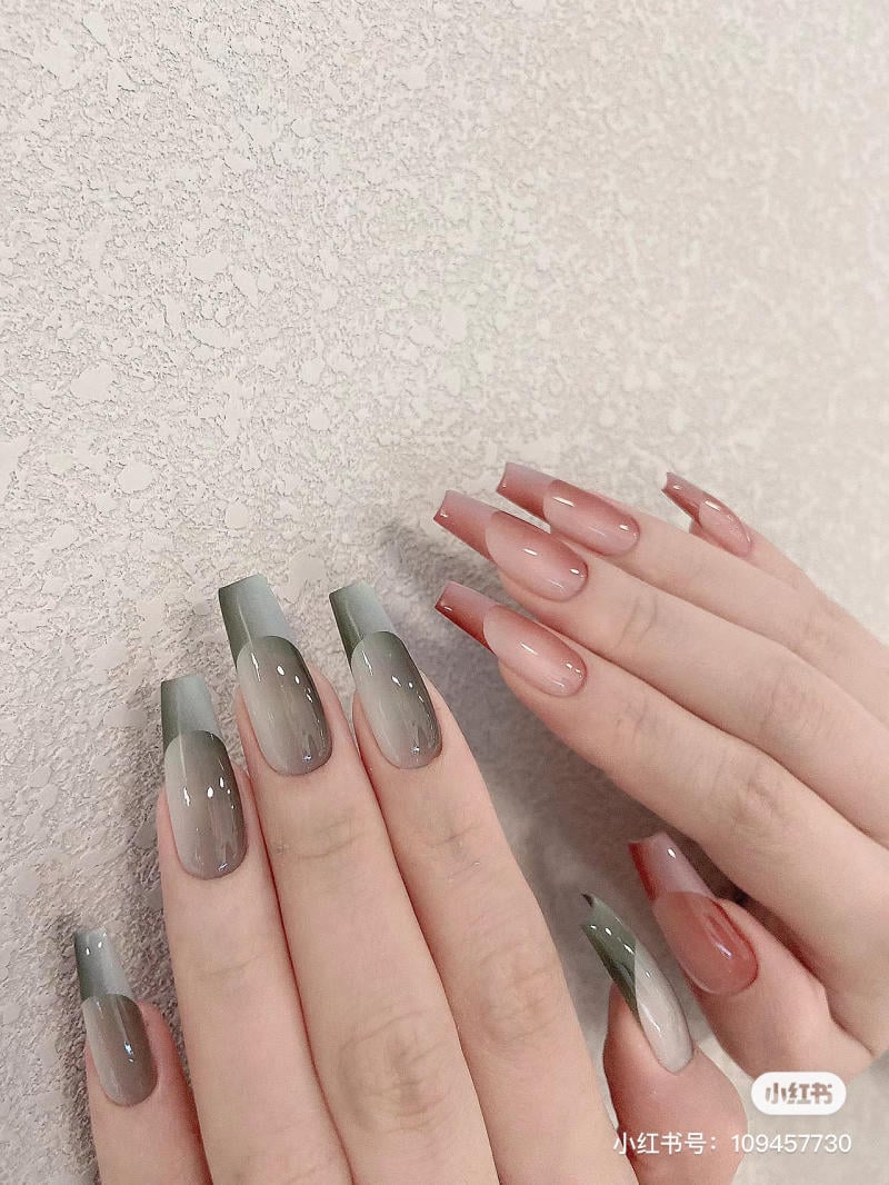 Hai bàn tay với móng tay dài, sơn màu xám và hồng, đặt trên nền tường có hoa văn.