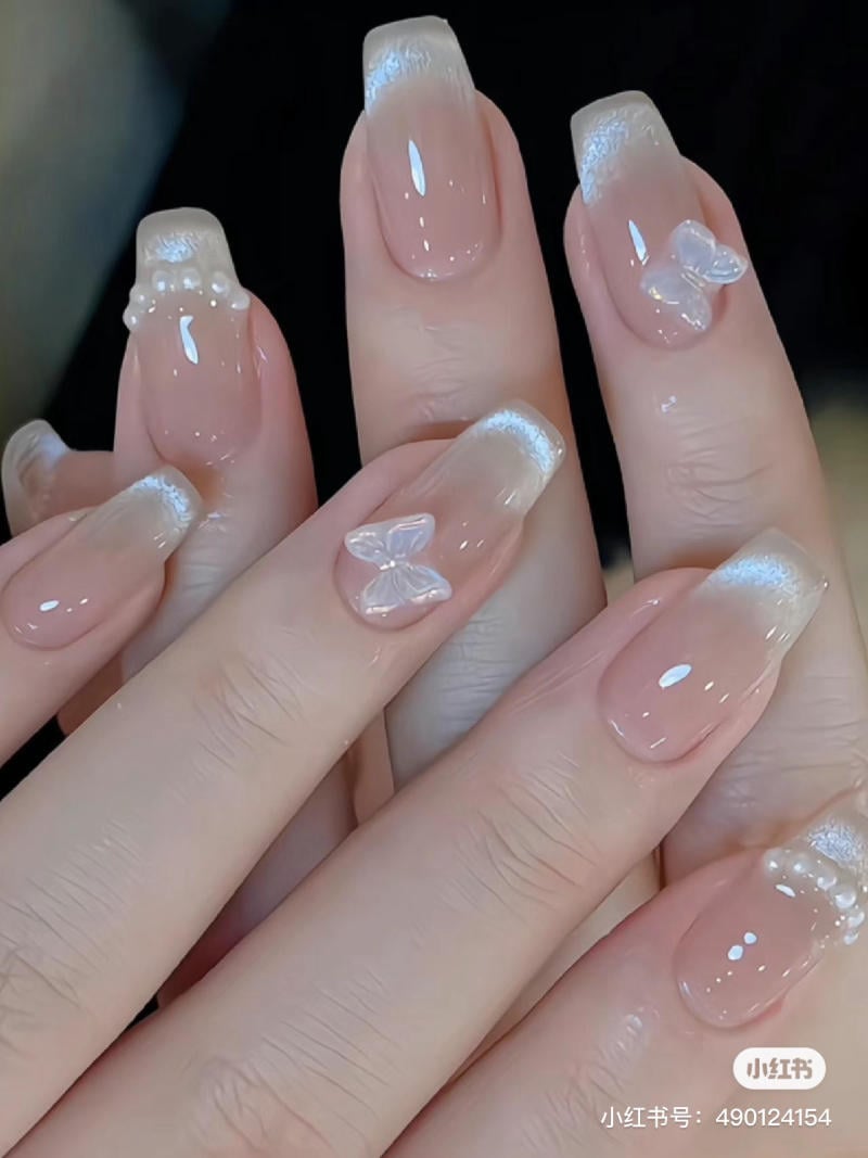 Bàn tay với móng tay được trang trí kiểu ombre, đính đá và họa tiết bướm, tạo vẻ đẹp tinh tế và sang trọng.