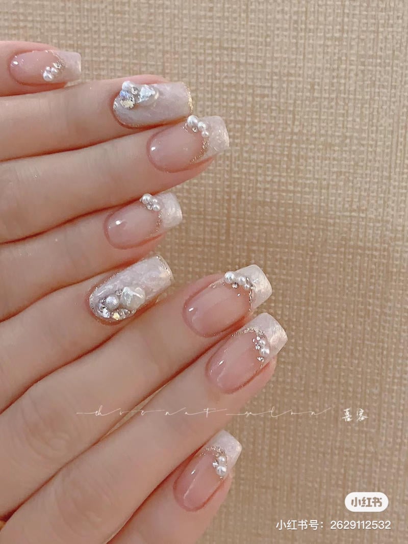 Bàn tay với móng tay được trang trí họa tiết hoa văn trắng và đính hạt sáng bóng.