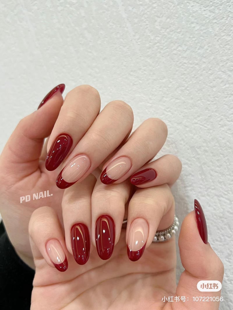 Bàn tay với móng tay được sơn kiểu Pháp đỏ, nền trắng, nhẫn bạc, trên nền tường sáng màu.