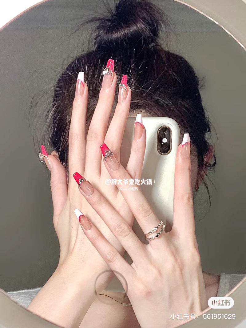 Người cầm điện thoại trước gương, móng tay được trang trí với màu sắc và họa tiết khác nhau.