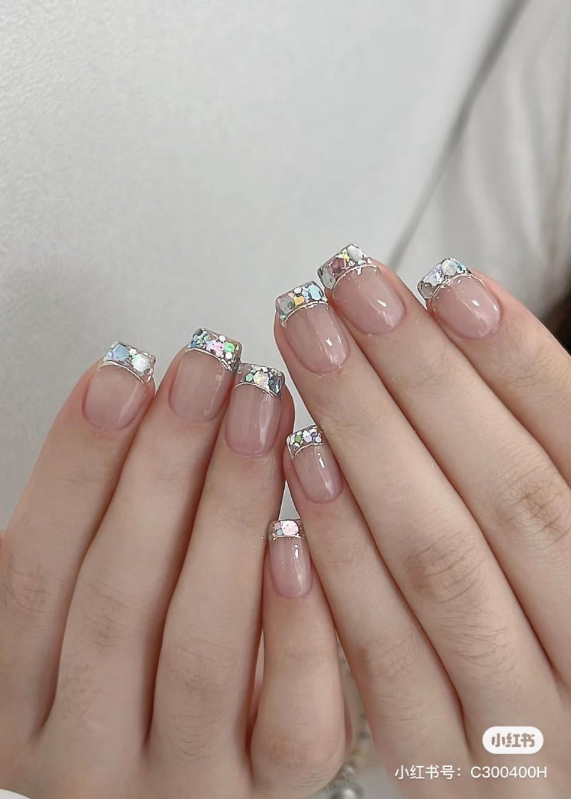 Bàn tay với móng tay được trang trí bằng sơn trong suốt và đính đá lấp lánh trên đầu móng.
