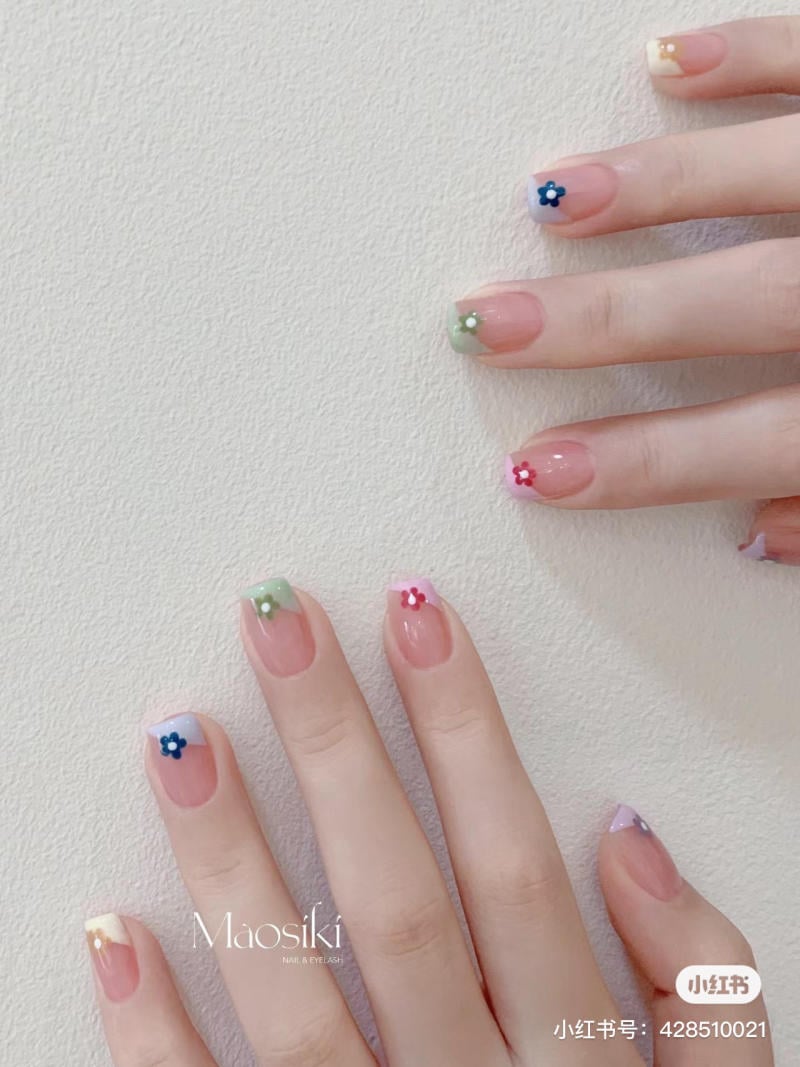 Bàn tay với móng tay được trang trí bằng sơn màu pastel và họa tiết hoa nhỏ trên nền trắng.