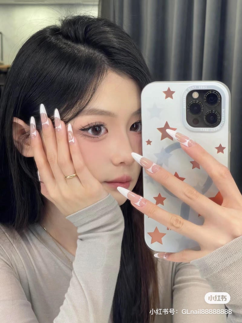 Người cầm điện thoại chụp ảnh tự sướng trước gương, móng tay dài và được trang trí tinh tế.
