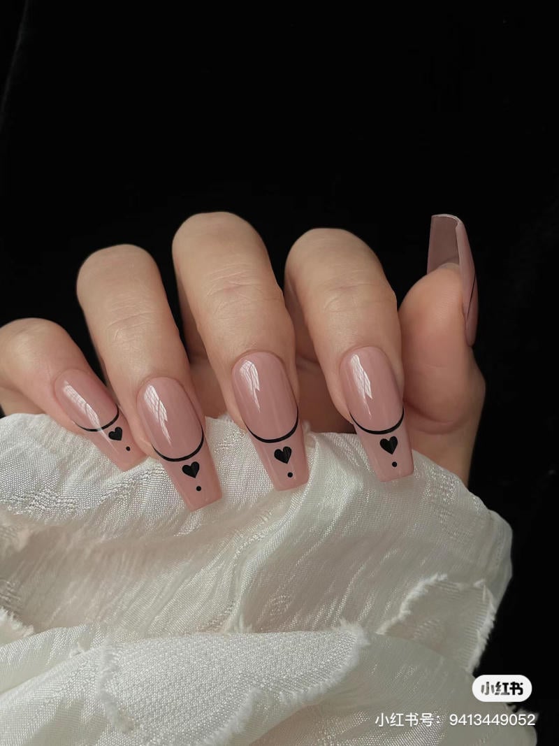 Bàn tay với móng tay được sơn màu nude, trang trí họa tiết trái tim và đường cong màu đen.