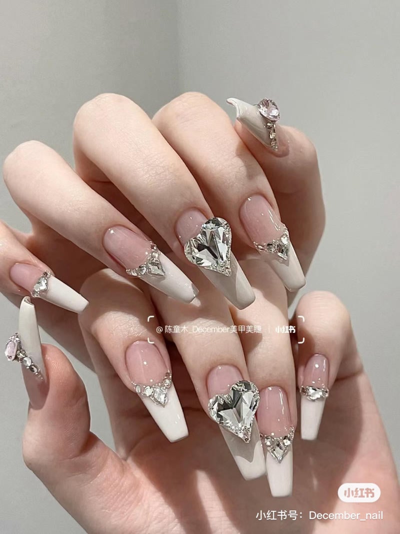 Bàn tay với móng tay dài, sơn màu trắng và trang trí đá lấp lánh hình trái tim.