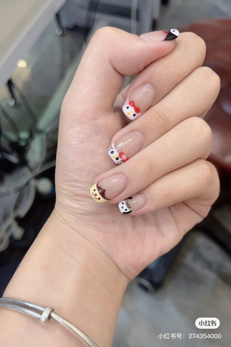 Bàn tay với móng tay trang trí hình mèo trên nền màu sắc khác nhau, được chụp trong không gian tiệm làm móng.