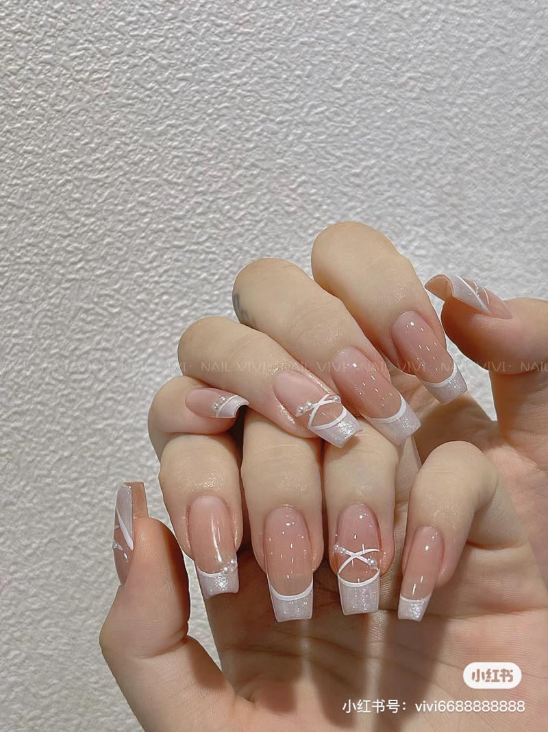 Bàn tay với móng tay dài, sơn màu nude, đầu móng trắng, trang trí họa tiết đơn giản.