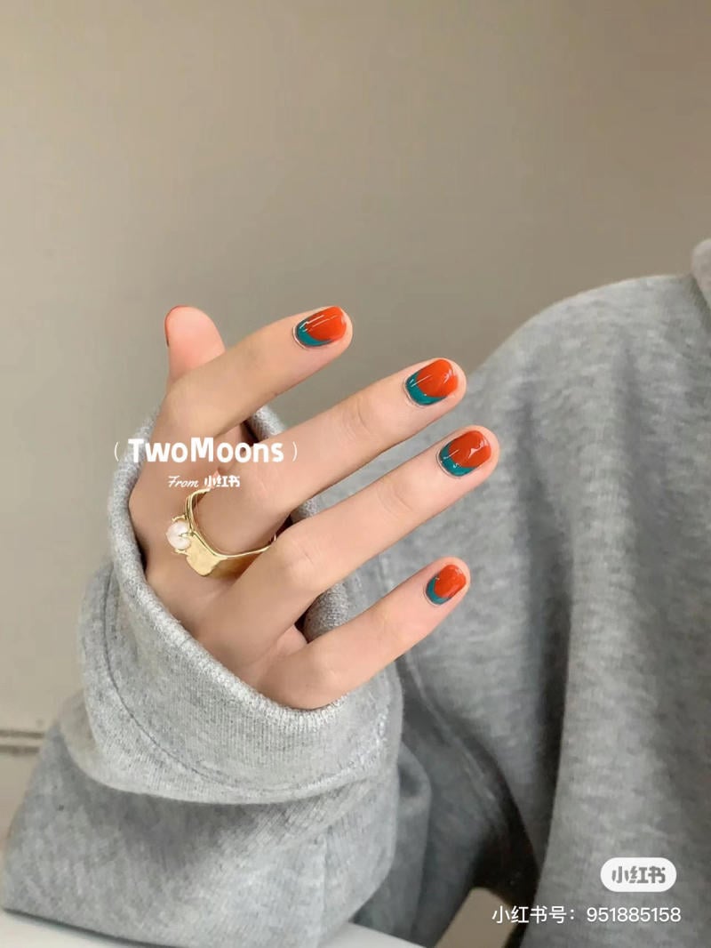Người đeo áo xám và nhẫn vàng, móng tay sơn màu cam và xanh lá.