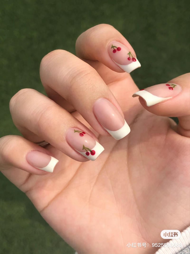Bàn tay với móng tay được sơn kiểu Pháp, trang trí họa tiết trái anh đào nhỏ trên nền xanh cỏ.