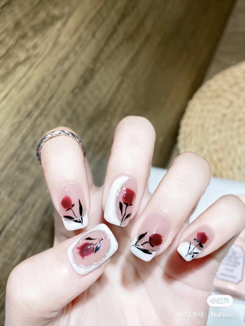 Bàn tay với móng tay được trang trí hoa văn màu đỏ và đen trên nền trắng, đặt trên bề mặt gỗ.