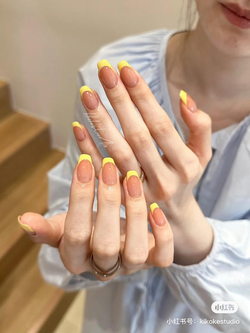 Người đang giơ hai bàn tay với móng tay được sơn màu vàng trên nền màu nude.