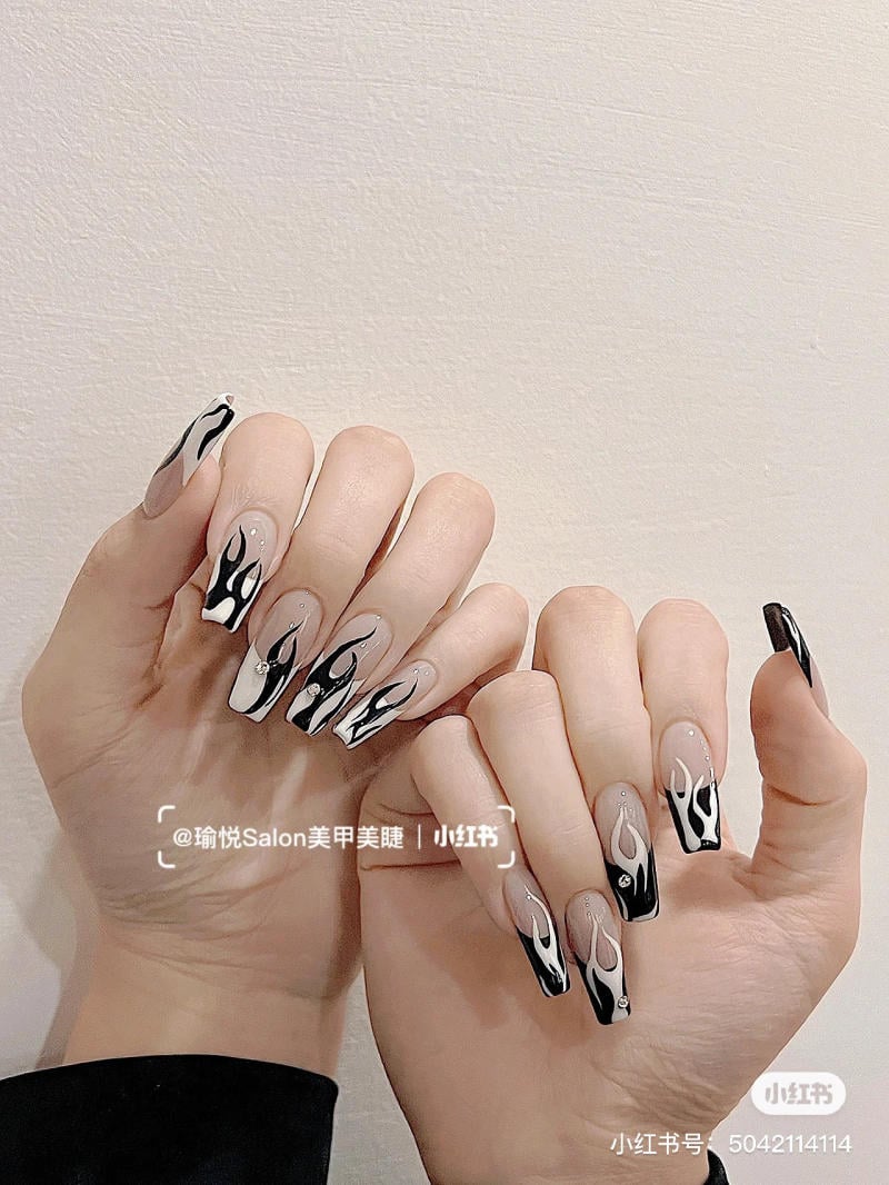 Bàn tay với móng tay dài được trang trí bằng họa tiết đen trắng và đính đá lấp lánh trên nền màu be.