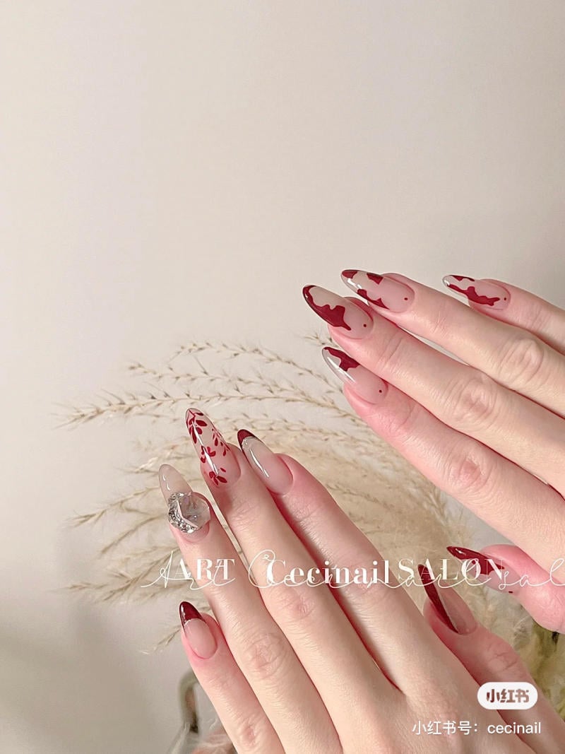 Bàn tay với móng tay được trang trí kiểu nghệ thuật, nền trắng, có hoa văn màu đỏ và bạc.