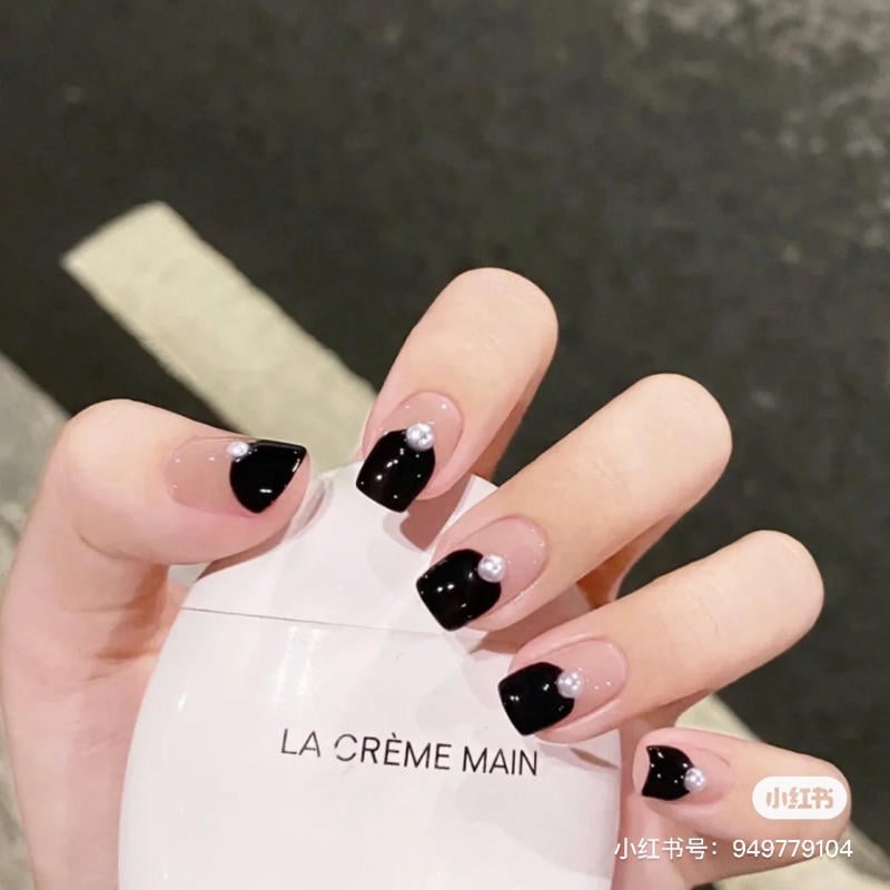 Bàn tay với móng tay đen có đính ngọc trai, cầm một sản phẩm có chữ "LA CRÈME MAIN".