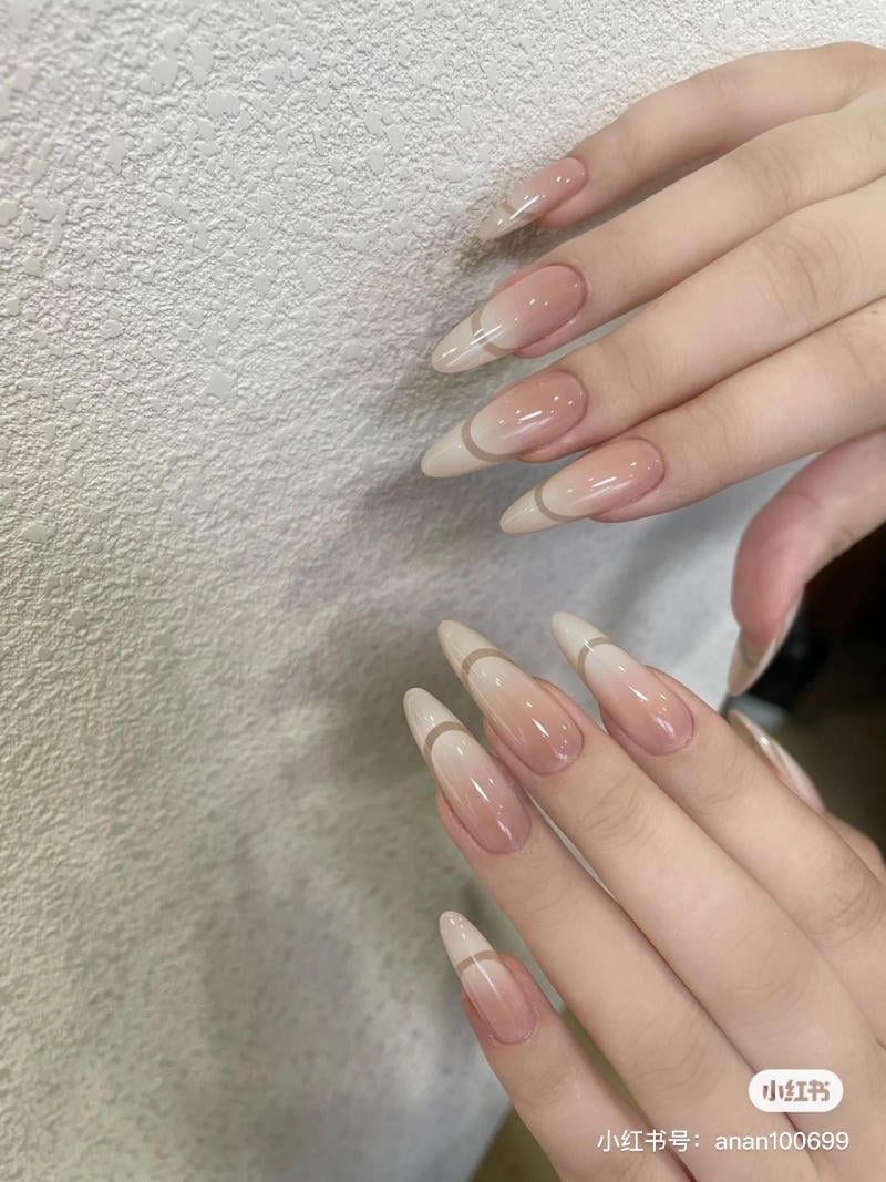 Bàn tay với móng tay dài, sơn màu ombre hồng và trắng, đặt trên nền tường màu trắng.