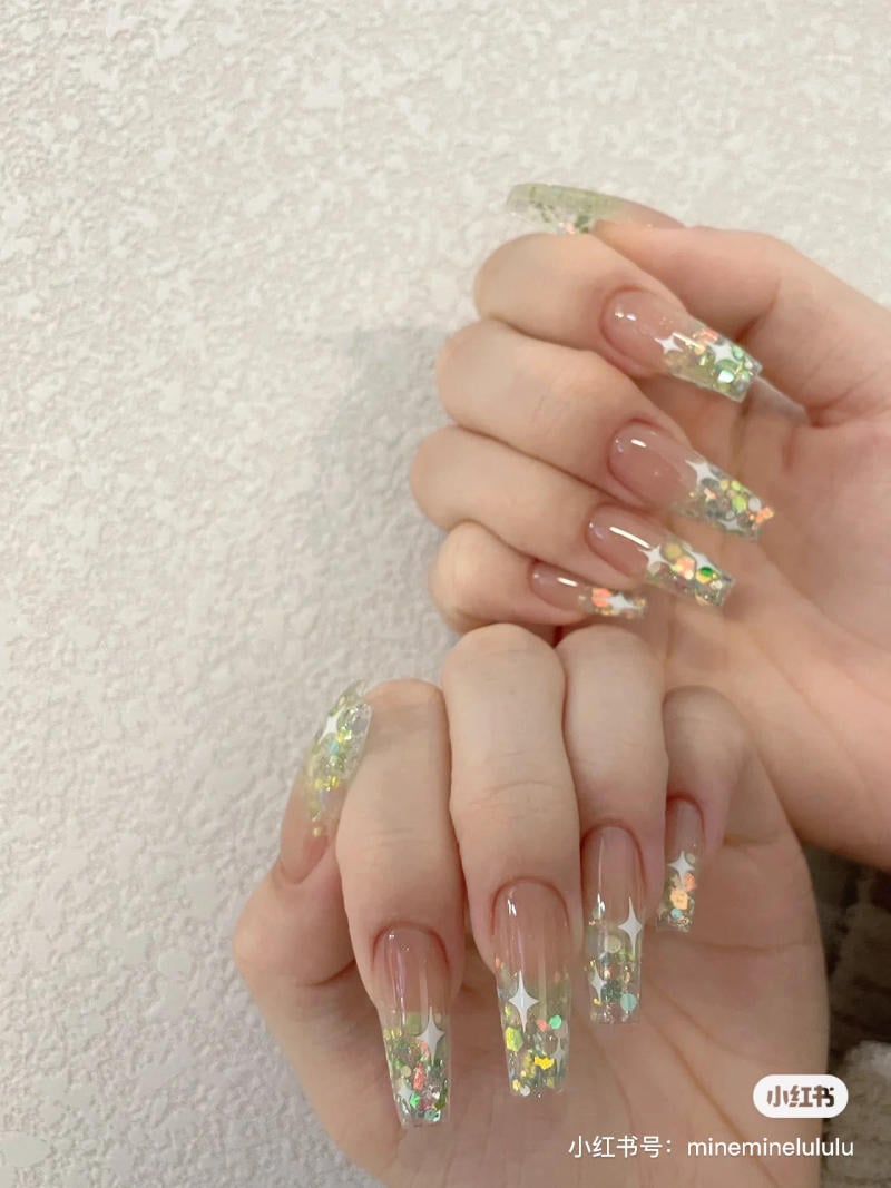 Bàn tay với móng dài, trang trí hoa văn lấp lánh nhiều màu sắc trên nền trắng.