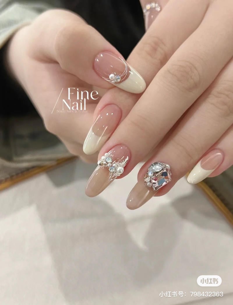 Móng tay dài trang trí đá quý và sơn màu nude kết hợp trắng, tạo điểm nhấn lấp lánh và sang trọng.