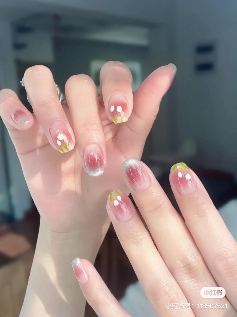 Bàn tay với móng tay được sơn màu hồng nhạt và họa tiết hoa trắng nhỏ, nền mờ.