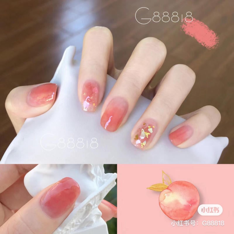 Bàn tay với móng tay sơn màu cam nhạt, có họa tiết trang trí ánh kim và hoa văn.