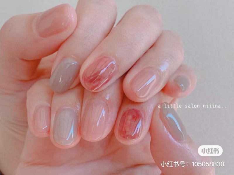 Bàn tay với móng tay được sơn màu hồng và xám, một số móng có họa tiết trang trí nhẹ nhàng.
