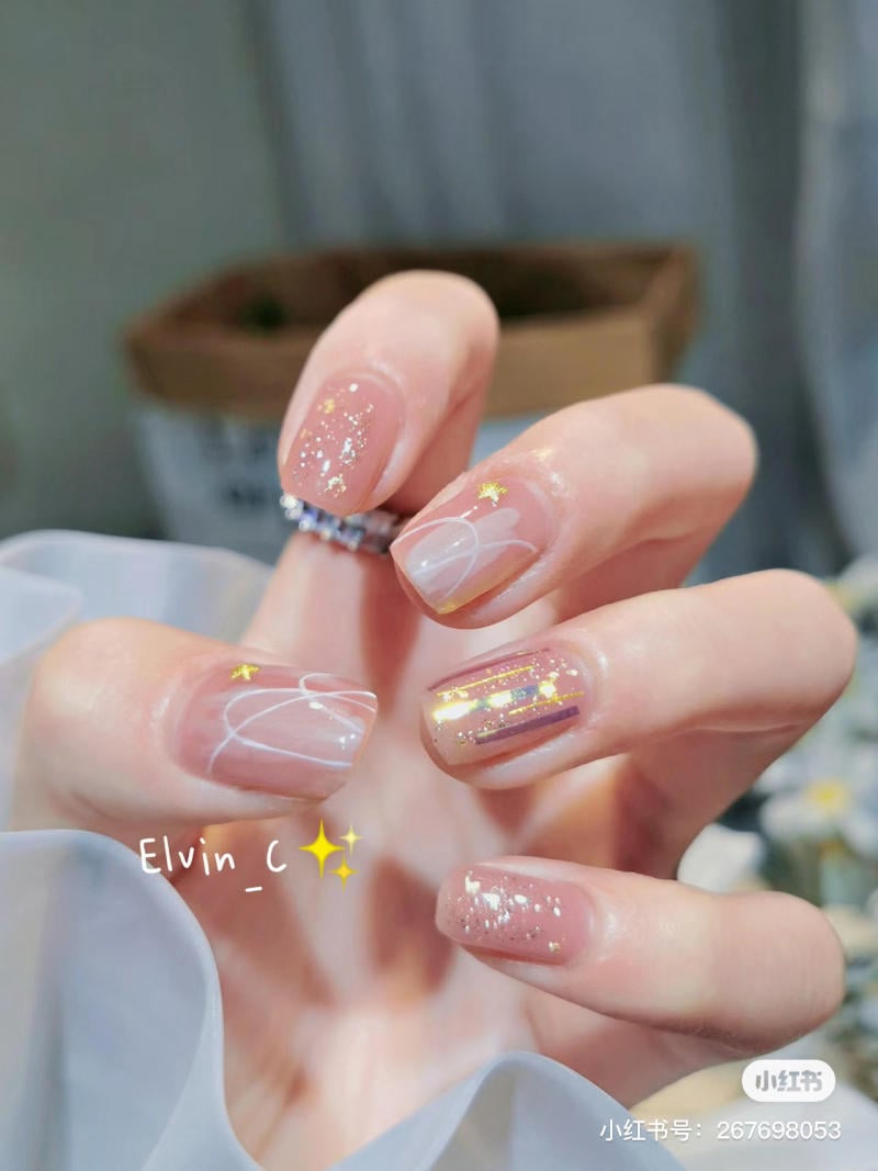 Bàn tay với móng tay được trang trí họa tiết lấp lánh và hoa văn tinh tế trên nền màu nude.