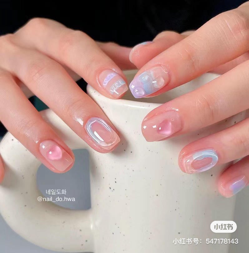 Bàn tay với móng tay được trang trí nhiều màu sắc pastel, đang cầm một chiếc cốc trắng.