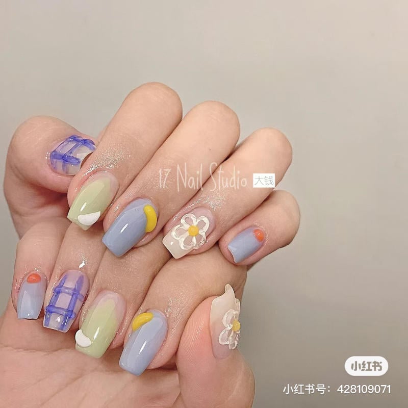Bàn tay với móng tay được trang trí đa sắc, họa tiết hoa và hình học, nền màu sáng.