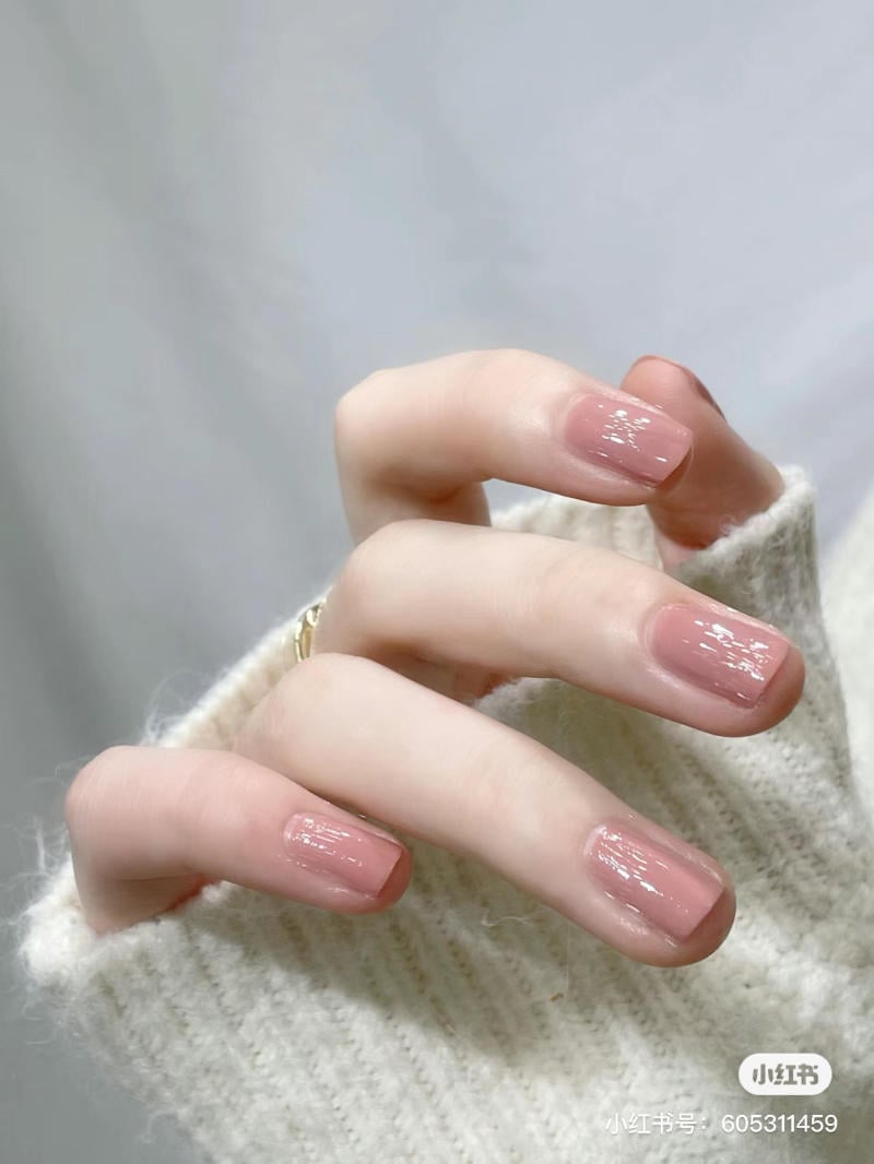 Bàn tay với móng tay sơn màu hồng nhạt, mặc áo len trắng, phông nền mờ.