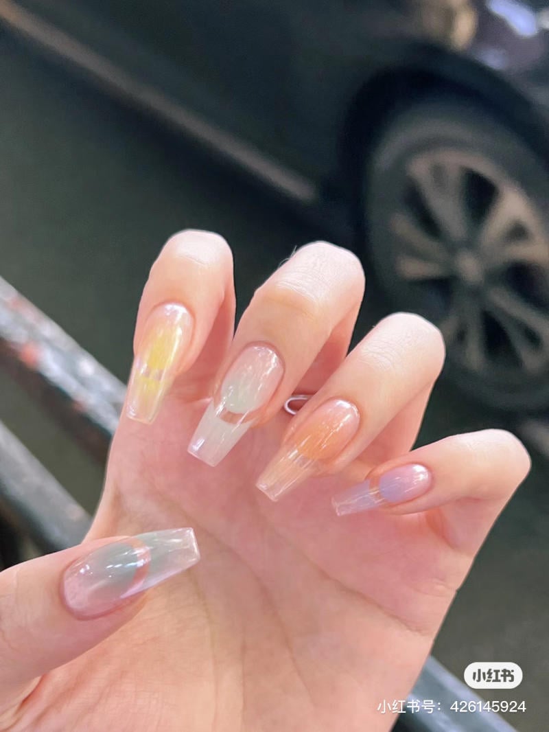 Bàn tay với móng tay dài được sơn màu pastel nhạt, chụp cận cảnh trong môi trường ngoài trời.