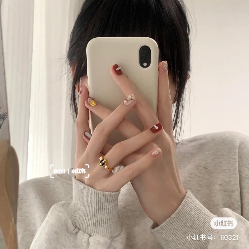 Người cầm điện thoại che mặt, móng tay sơn nhiều màu sắc và đeo nhẫn vàng.