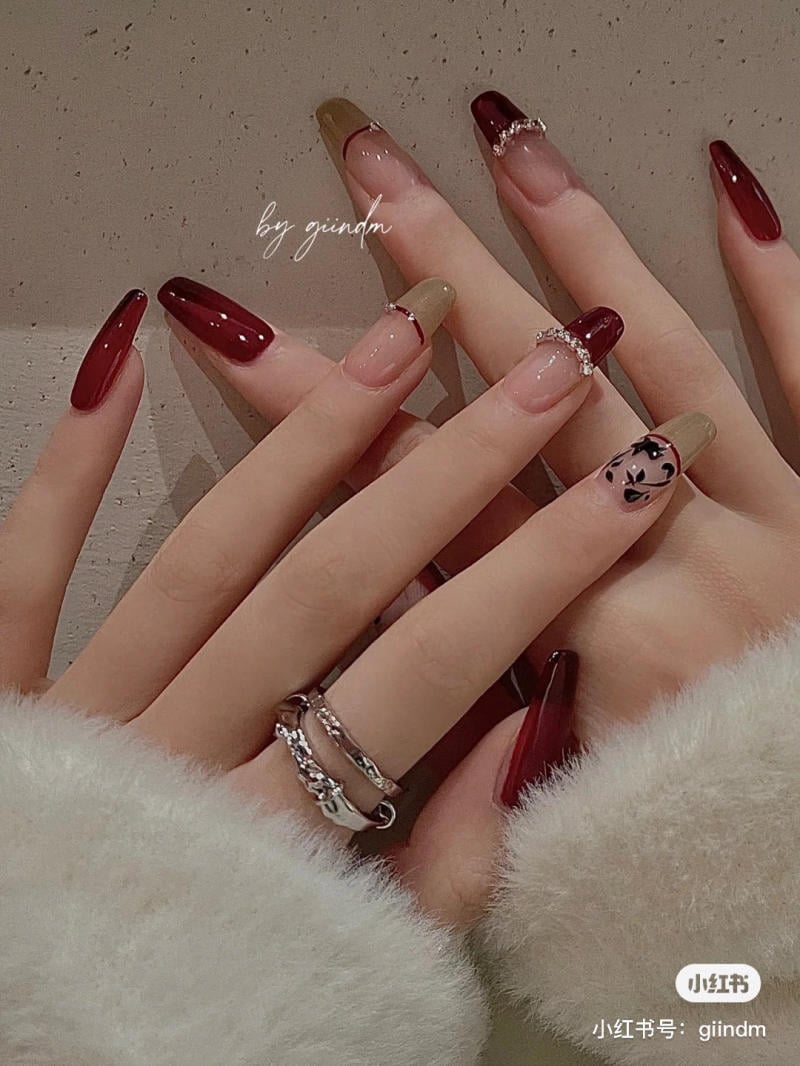 Bàn tay với móng tay dài và sắc màu đỏ, vàng, trang trí họa tiết và đính đá, đeo nhẫn bạc.