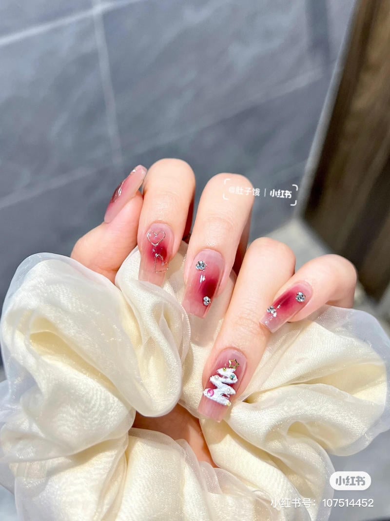 Bàn tay cầm dây buộc tóc, móng tay được sơn màu hồng, trang trí họa tiết cây thông Noel và đá lấp lánh.