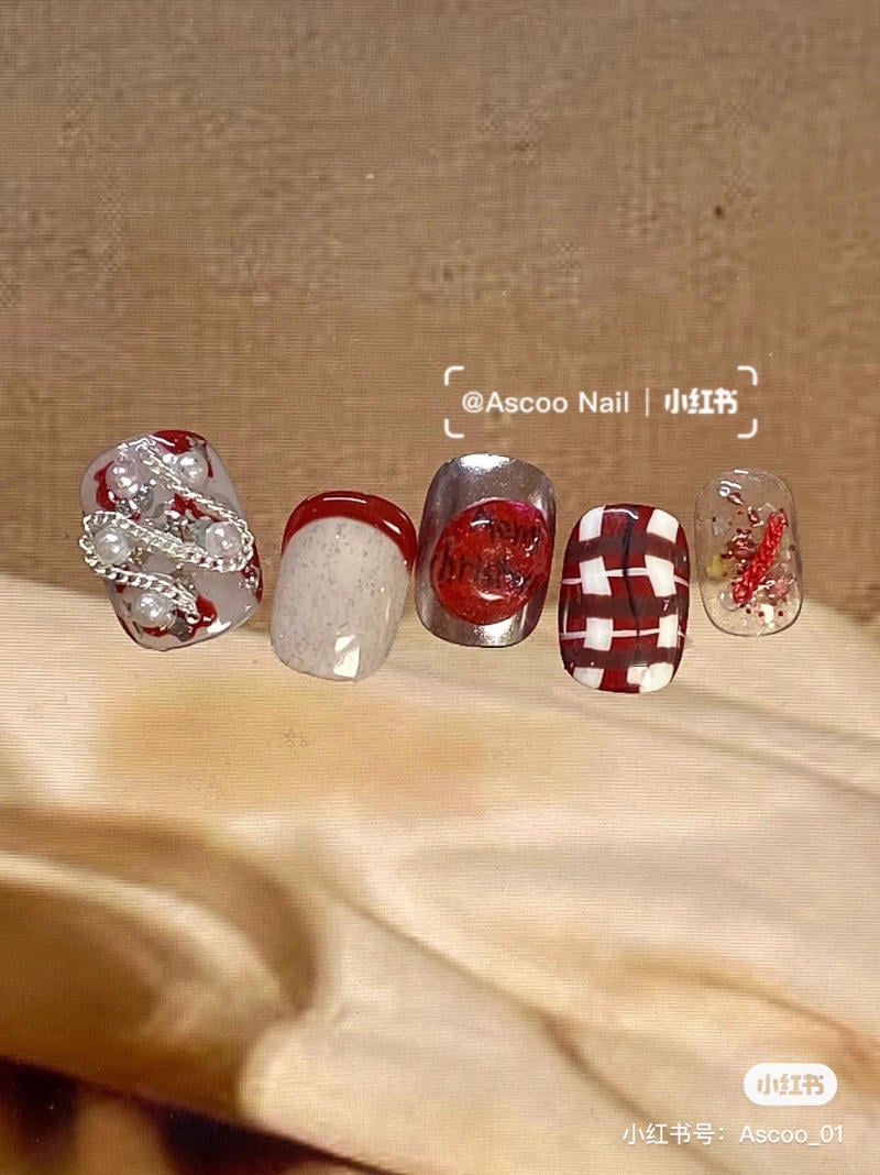 Bộ móng giả với thiết kế đa dạng, kết hợp màu đỏ, trắng và bạc, có họa tiết nổi bật và đính hạt trang trí.