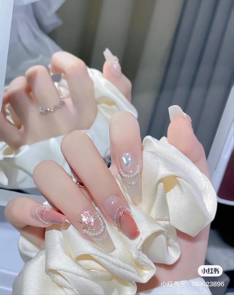 Bàn tay với móng tay được trang trí cầu kỳ, cầm một chiếc vải lụa trắng trước gương.