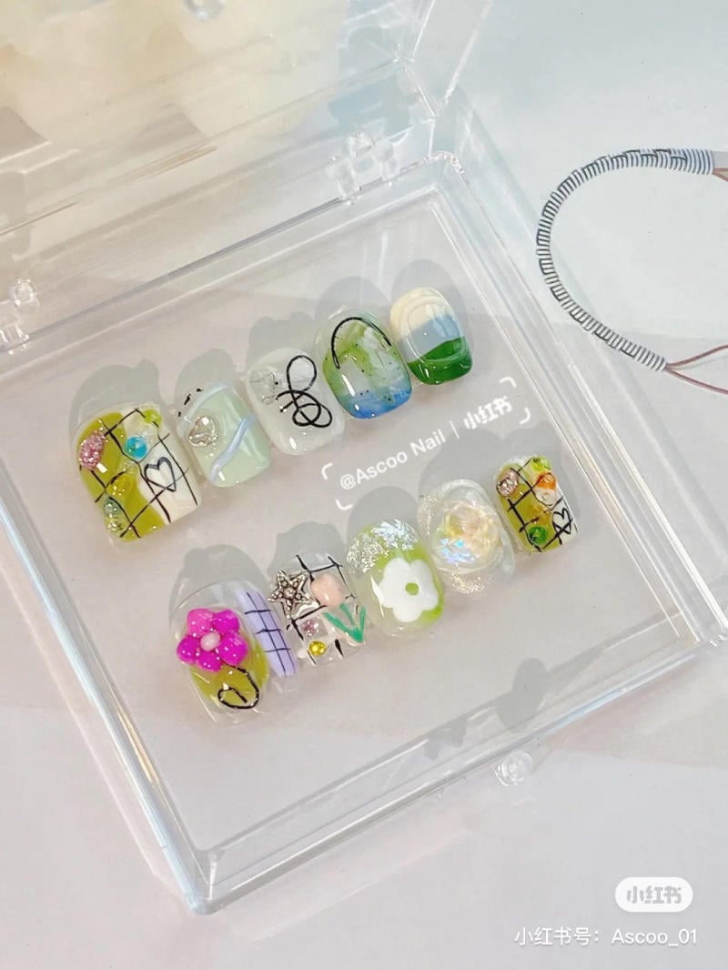 Bộ móng giả trang trí đa dạng họa tiết và màu sắc, đặt trong hộp nhựa trong suốt.