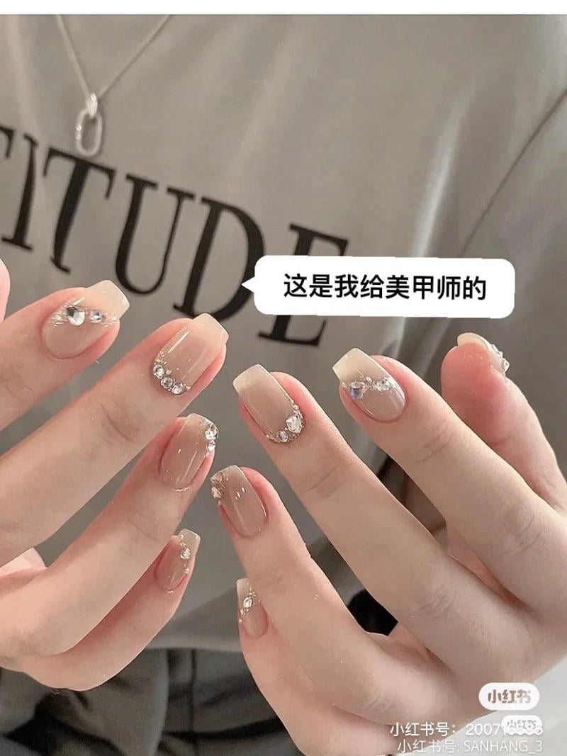 Hai bàn tay với móng tay được sơn màu nude và trang trí đá lấp lánh.