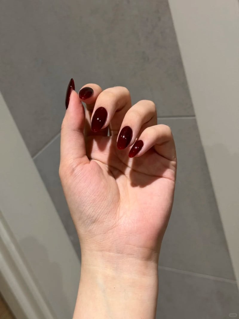 Bàn tay với móng tay sơn màu đỏ sẫm, nền gạch xám nhạt.