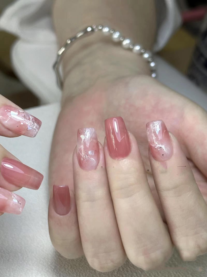 nail-van-da-dep__11__44c233897250423398eb563cf8418118 Bàn tay với móng tay sơn màu hồng nhạt, một số móng có họa tiết trang trí tinh tế.