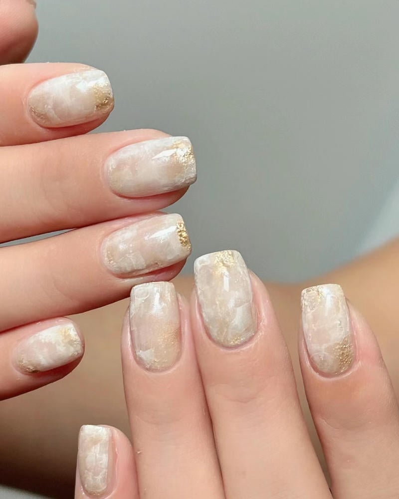 nail-van-da-dep__13__50950f4754f046809ac893fd0dcc0314 Bàn tay với móng tay được sơn màu trắng và vàng, thiết kế hoa văn đá cẩm thạch.