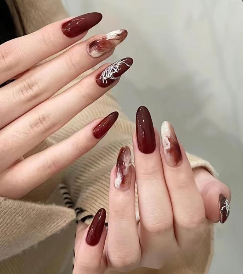 nail-van-da-dep__26__02ef1afc09764304ac07810a31746e56 Bàn tay với móng tay dài sơn màu đỏ, trang trí hoa văn trắng và màu nâu nhạt.