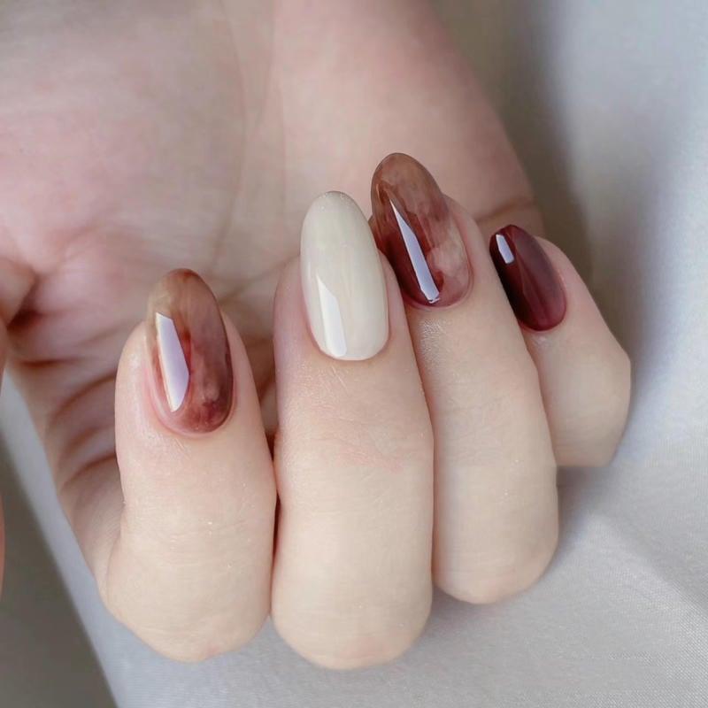 nail-van-da-dep__31__a75bf0718e644c2a8c9309fafaf11e1f Bàn tay với móng tay được sơn màu trắng và nâu, tạo kiểu ombre bóng, nền vải trắng mờ.