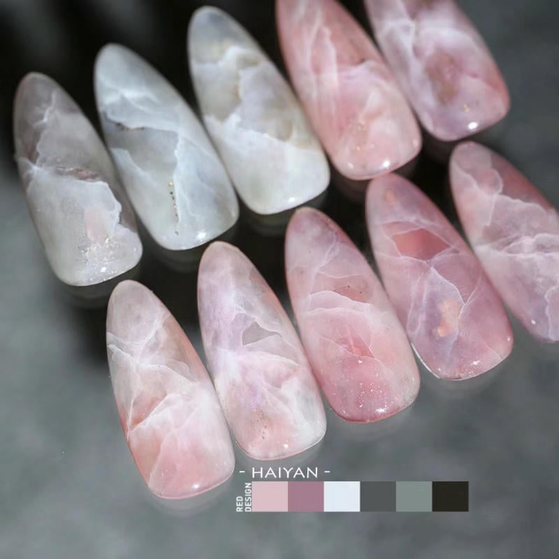 nail-van-da-dep__33__49aa77aedd72461baf0283a63b2b9de4 Bộ móng giả màu hồng và trắng với hoa văn đá cẩm thạch, hiển thị trên bề mặt tối.