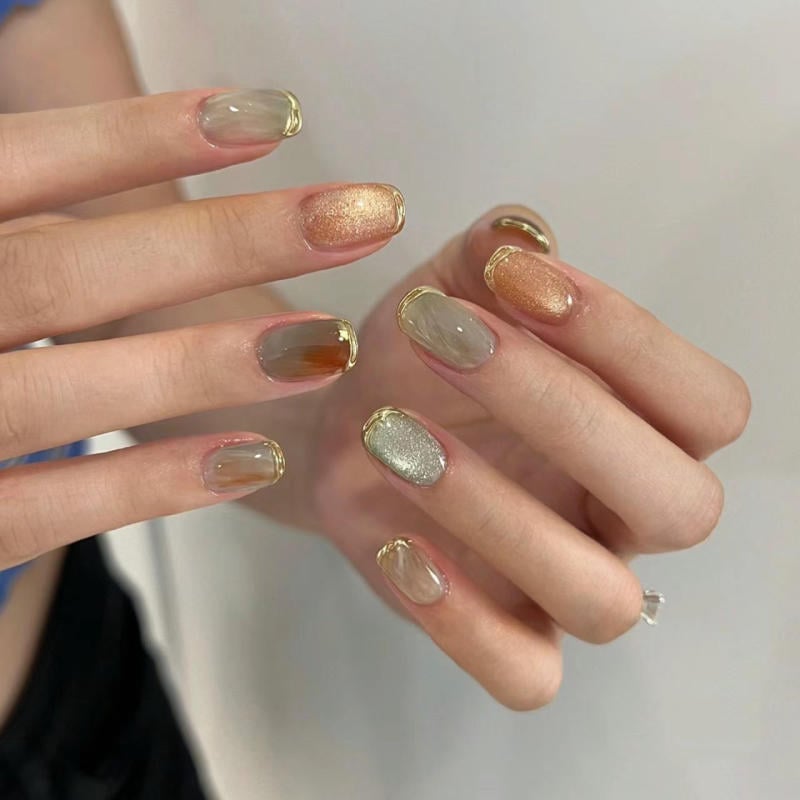 nail-van-da-dep__40__8b511907f1e74a5cb4e23701154aa04e Bàn tay với móng tay được sơn màu đa dạng, ánh kim và viền vàng, nền trắng nhạt.
